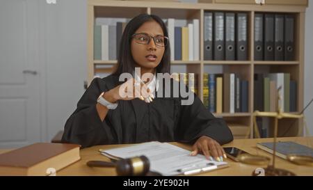 Richterin mit Brille und schwarzem Gewand am Schreibtisch mit Hammer und juristischen Dokumenten im Gerichtssaal Stockfoto