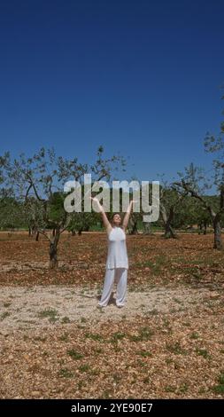 Eine junge, schöne hispanische Frau steht fröhlich unter Olivenbäumen in apulien, italien, unter einem klaren blauen Himmel und umrahmt die natürliche Schönheit um sie herum. Stockfoto