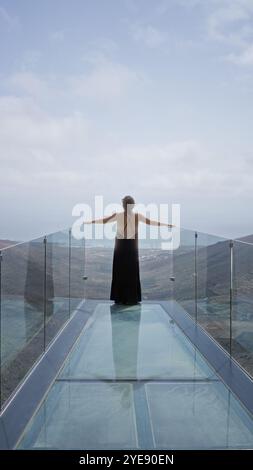 Frau Sightseeing im Freien in haria lanzarote auf einer Glasbrücke mit ausgebreiteten Armen mit Blick auf die atemberaubende Landschaft der kanarischen Inseln unter Stockfoto