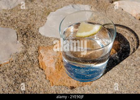 Ein Glas mit Sprudelwasser oder Tonic Water, mit einer Scheibe Zitrone und Eiswürfeln, auf einer rustikalen Stein- und Mörteloberfläche Stockfoto