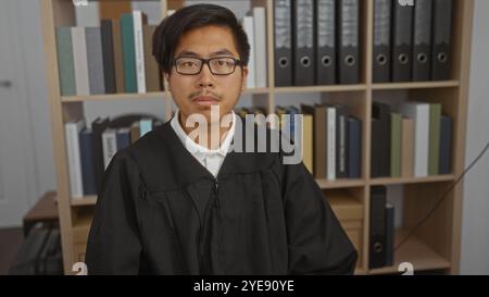 Junger Mann in richterlichem Gewand, der in einem Büro mit Büchern und Ordnern sitzt und ein professionelles und seriöses Umfeld repräsentiert. Stockfoto