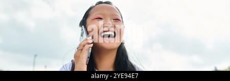 Eine fröhliche Studentin lacht fröhlich, während sie am Telefon spricht und einen sonnigen Tag im Freien genießt. Stockfoto