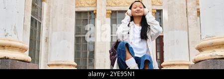 Eine stilvoll gekleidete junge Frau entspannt sich auf den Stufen der Universität und genießt einen Moment der Ruhe und der Jugendkultur. Stockfoto