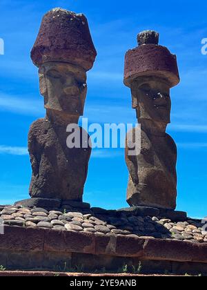 Zwei Moai-Statuen mit roten Pukao-Kopfbedeckungen in Ahu Tongariki auf der Osterinsel, Chile, stehen unter einem blauen Himmel und symbolisieren die alte Rapa Nui-Kultur. Stockfoto