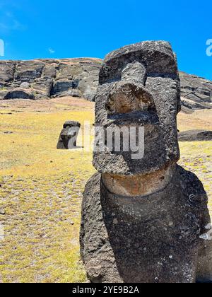 Zwei Moai-Statuen auf der Osterinsel, Chile, vor einer felsigen Landschaft und blauem Himmel. Diese antiken Schnitzereien gehören zum UNESCO-Weltkulturerbe Stockfoto