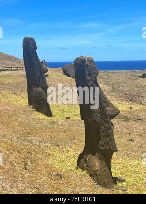 Zwei Moai-Statuen im Steinbruch Rano Raraku auf der Osterinsel, Chile, mit Blick auf den Pazifischen Ozean unter blauem Himmel. UNESCO-Weltkulturerbe. Stockfoto