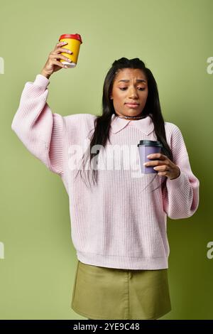 Eine stilvolle junge Frau hat Schwierigkeiten, zwei Kaffeetassen auszubalancieren, während sie für den Herbst angezogen ist. Stockfoto