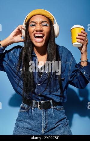 Eine stilvolle junge Frau mit Kopfhörern lächelt hell, während sie eine Kaffeetasse hält. Stockfoto