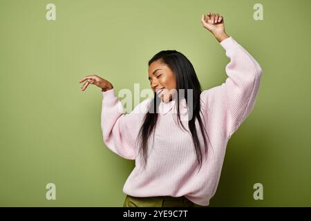 Eine junge Frau tanzt fröhlich in stilvoller Herbstmode vor grünem Hintergrund. Stockfoto