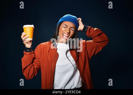 Eine junge Frau in kuscheliger Herbstkleidung hält glücklich ein warmes Getränk und feiert die Saison. Stockfoto