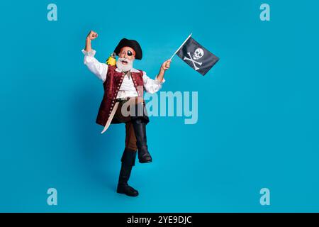 Foto in voller Länge von älteren lustigen Piraten Opa gewinnen Wellenflagge tragen Maskerade Party Kostüm isoliert blau Hintergrund Stockfoto