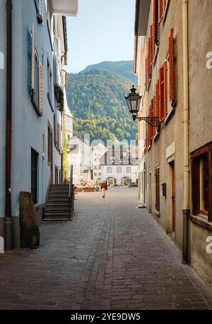 Eine enge Straße führt zum Arcas-Platz. Stadtstraße mit alten mittelalterlichen Häusern, die mit Laternen und Fensterläden dekoriert sind, wald auf dem Hügel im Hintergrund. Stockfoto