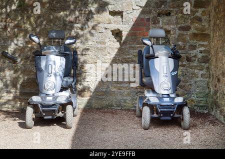 Zwei Mobilitätswagen, Roller für Behinderte, parken neben einer alten rustikalen Ziegelmauer. Stockfoto