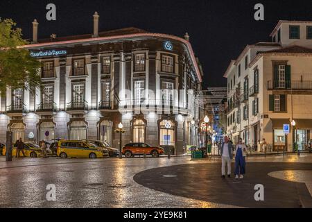 Fußgänger überqueren einen Stadtplatz mit beleuchteten Gebäuden bei Nacht in Funchal auf der Insel Madeira, Portugal; Funchal, Madeira, Portugal Stockfoto