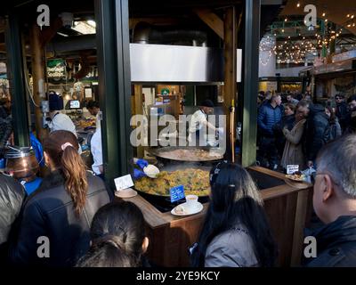 Essensstand mit Paella und Kunden, die auf Borough Market, London, Großbritannien, warten Stockfoto