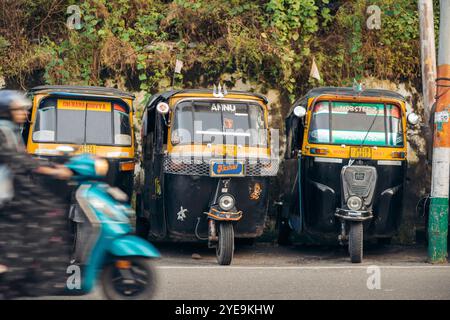 Auto-Rikschas parkten in einer Reihe entlang einer Straße mit einer Frau, die auf einem Motorroller vorbeifuhr, in Jammu, Indien; Jammu, Jammu und Kaschmir, Indien Stockfoto