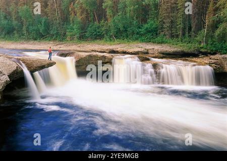 Frau steht auf einem Felsvorsprung mit Blick über die Coral Falls im Sambaa Deh Falls Territorial Park in den Nordwest-Territorien Kanadas Stockfoto