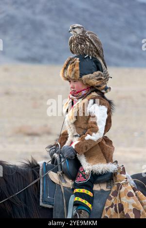 Junger Zuschauer zu Pferd mit dem Goldenen Adler (Aquila chrysaetos), der die mongolischen Adlerjäger beim Adlerfest in der Mongolei beobachtet. Der Adler... Stockfoto