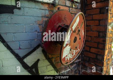Rostiger alter roter Metallschlauchhaspel an der Wand einer verlassenen Fabrik Stockfoto