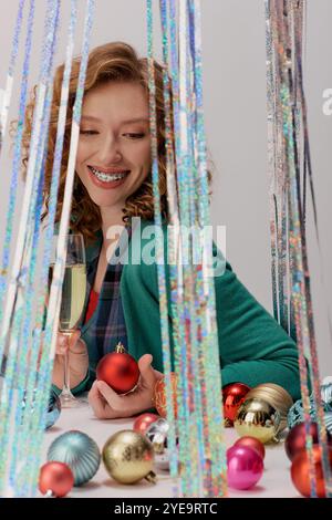 Eine junge Frau posiert fröhlich, umgeben von farbenfrohen Weihnachtsschmuck und Dekor. Stockfoto