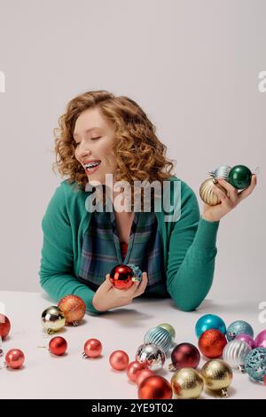 Eine junge Frau posiert fröhlich mit lebendigen Ornamenten, während sie lächelt und den Feiertagsgeist genießt. Stockfoto