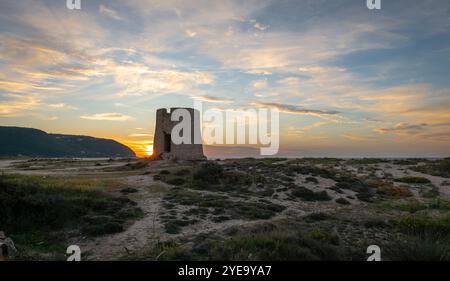 Eine alte Steinwindmühle am Strand bei Sonnenuntergang mit atemberaubendem Sonnenlicht und Wolken. Stockfoto