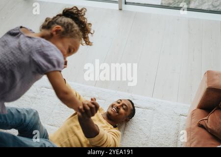 Blick auf einen glücklichen Mann, der mit seiner Tochter spielt, während er zu Hause auf dem Teppich liegt Stockfoto