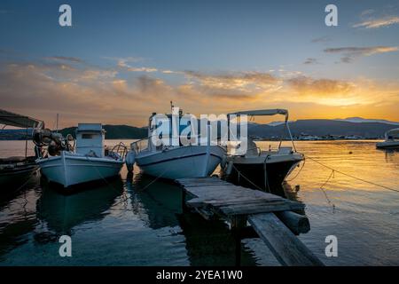 Kleine Boote, die an einem Morgen mit einem wunderschönen goldenen Sonnenaufgang und Wolken in einem Hafen vor Anker liegen. Stockfoto