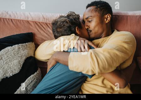 Vater küsst den Sohn, während er zu Hause auf dem Sofa sitzt Stockfoto