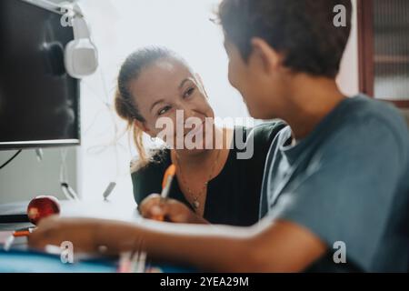 Lächelnde Mutter hilft dem Sohn, Hausaufgaben zu Hause zu machen Stockfoto