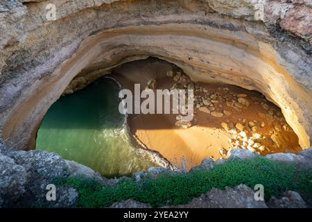 Hochwinkelansicht des warmen Sonnenuntergangs auf Sand, Felsen und Wasser in der Benagil-Höhle entlang der Küste Portugals; Lagoa, Faro, Portugal Stockfoto