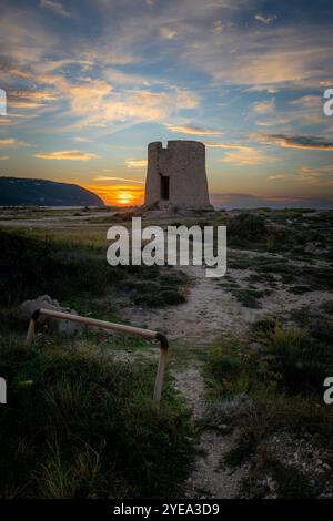 Eine alte Steinwindmühle am Strand bei Sonnenuntergang mit atemberaubendem Sonnenlicht und Wolken. Stockfoto