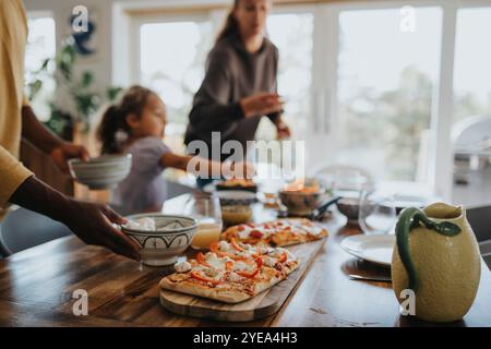 Frisch gebackene Pizza, die während des Mittagessens zu Hause auf dem Esstisch gehalten wird Stockfoto