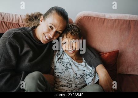 Hochwinkelporträt der Mutter mit Arm um den Sohn, der zu Hause auf dem Sofa sitzt Stockfoto
