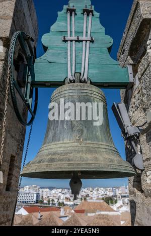 Nahaufnahme einer verwitterten Glocke an der Kathedrale von Faro (Kathedrale der Heiligen Maria) mit einem Stadtbild von Faro, Portugal im Hintergrund. Faro ist die Hauptstadt ... Stockfoto