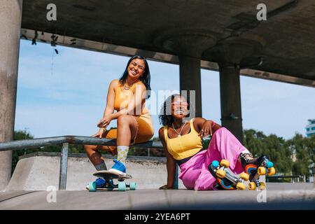 Porträt glücklicher Freundinnen mit Rollschuhen, die an sonnigen Tagen in der Nähe der Überführung sitzen Stockfoto