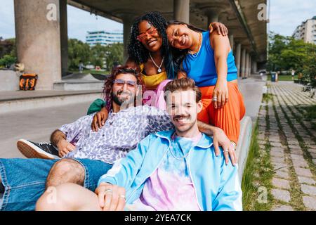 Porträt glücklicher modischer männlicher und weiblicher Freunde, die in der Nähe der Überführung unter der Brücke sitzen Stockfoto