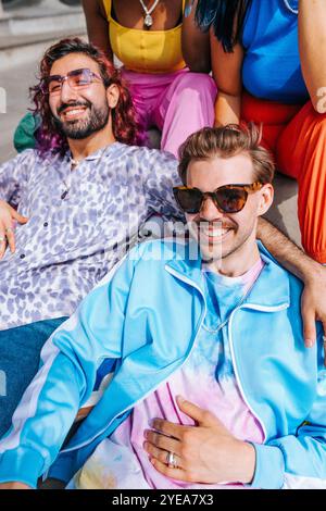 Porträt eines lächelnden, modischen Mannes, der mit männlichen und weiblichen Freunden an sonnigem Tag sitzt Stockfoto