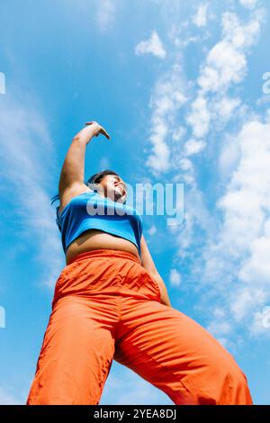 Tiefwinkelansicht einer glücklichen Frau, die unter bewölktem Himmel tanzt Stockfoto