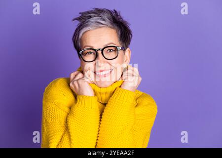 Foto-Porträt der attraktiven Reifen Frau Touch Rollkragen Wärme gekleidet stilvolle gelbe Kleidung isoliert auf lila Farbe Hintergrund Stockfoto