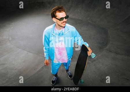 Lächelnder, modischer Mann in Casuals, der mit Longboard auf der Überführungsstraße steht Stockfoto