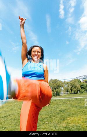 Fröhliche junge Frau, die die Zunge ausstreckt, während sie im Park unter blauem Himmel genießt Stockfoto