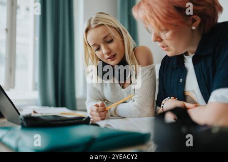 Blondes Mädchen mit kabellosen Kopfhörern, die Buch lesen, mit nicht-binären Personen im Unterricht Stockfoto