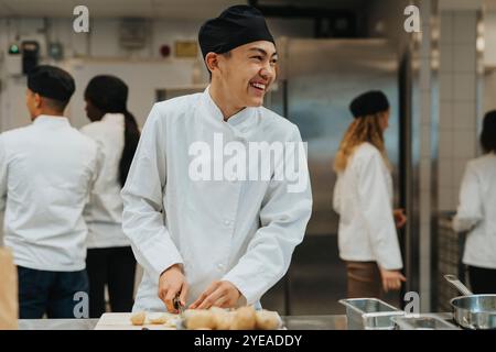 Glücklicher männlicher Teenager-Praktikant, der Essen in der kommerziellen Küche hackt Stockfoto