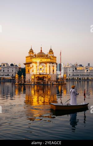 Goldener Tempel, ein Sikh Gurdwara, mit einem Mann, der in einem Boot im Pool in der Dämmerung steht und paddelt, in Amritsar, Punjab, Indien Stockfoto