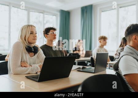 Blondes Mädchen und Teenager sitzen mit Laptops am Schreibtisch im Klassenzimmer Stockfoto