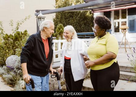 Glücklicher Seniorenmann und Frau mit weiblicher Betreuerin in der Nähe des Altersheims Stockfoto