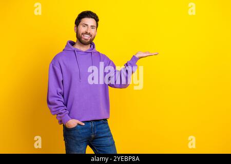 Foto-Porträt des netten jungen männlichen Haltes leerer Raum gekleidet stilvolle violette Kleidung isoliert auf gelbem Farbhintergrund Stockfoto