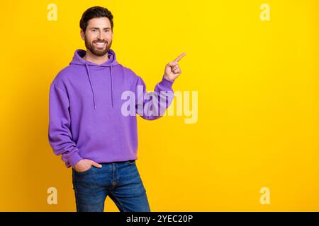 Foto-Porträt des netten jungen männlichen Punktes leerer Raum gekleidet stilvolles violettes Kleid isoliert auf gelbem Farbhintergrund Stockfoto