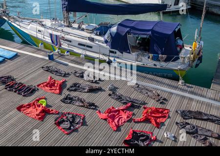 Wasserdichte und wetterfeste Segelkleidung, die auf einem Ponton in einem Yachthafen neben einer großen Seeschifffahrt-Yacht in einem Yachthafen an den gunwharf-Kais trocknet. Stockfoto